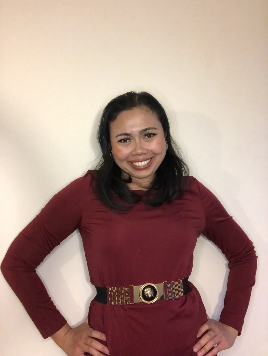 Krittaya smiling with her hands on her hips, wearing a burgundy dress