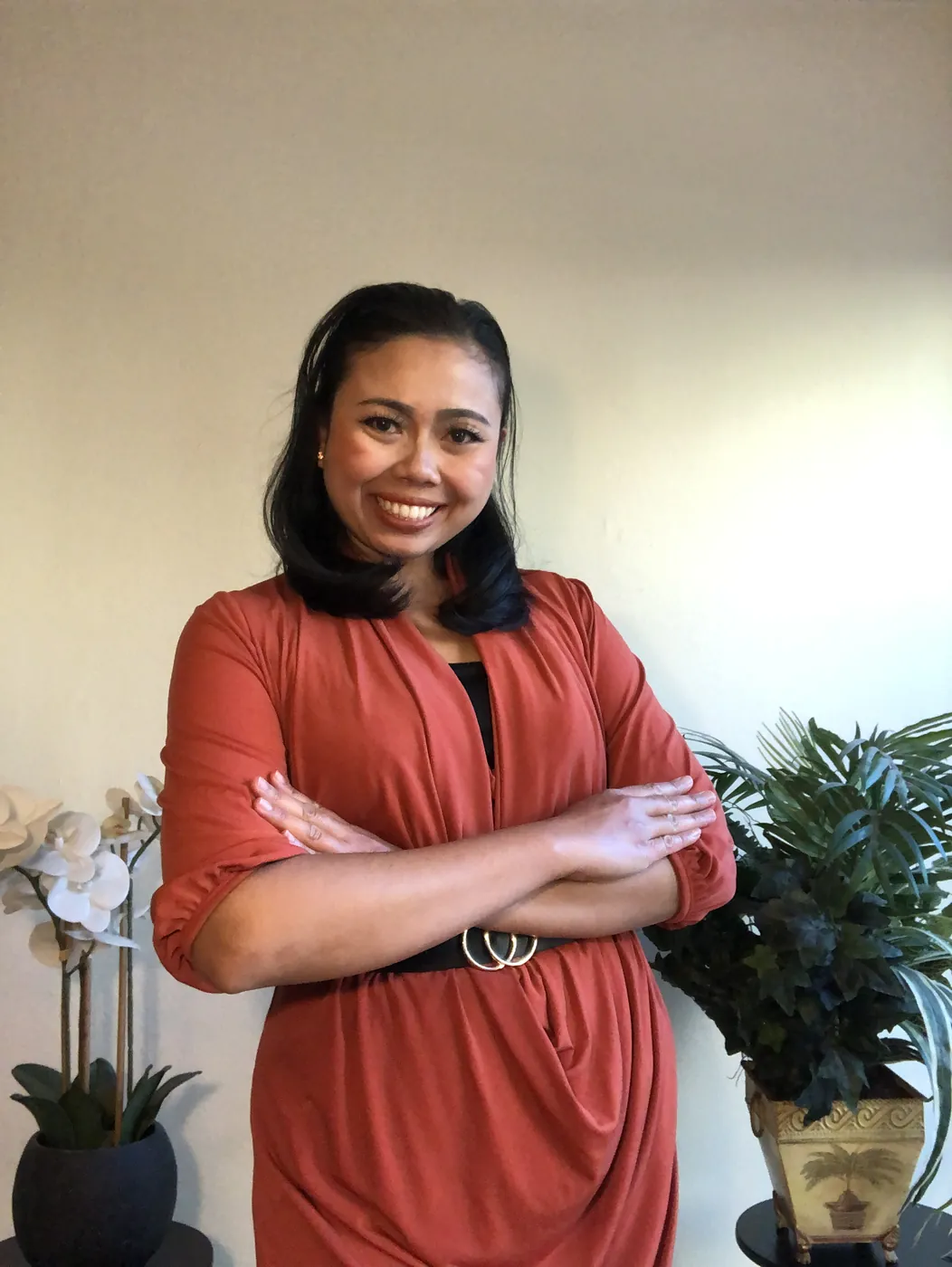 Krittaya smiling with her arms crossed, wearing a rust-coloured dress