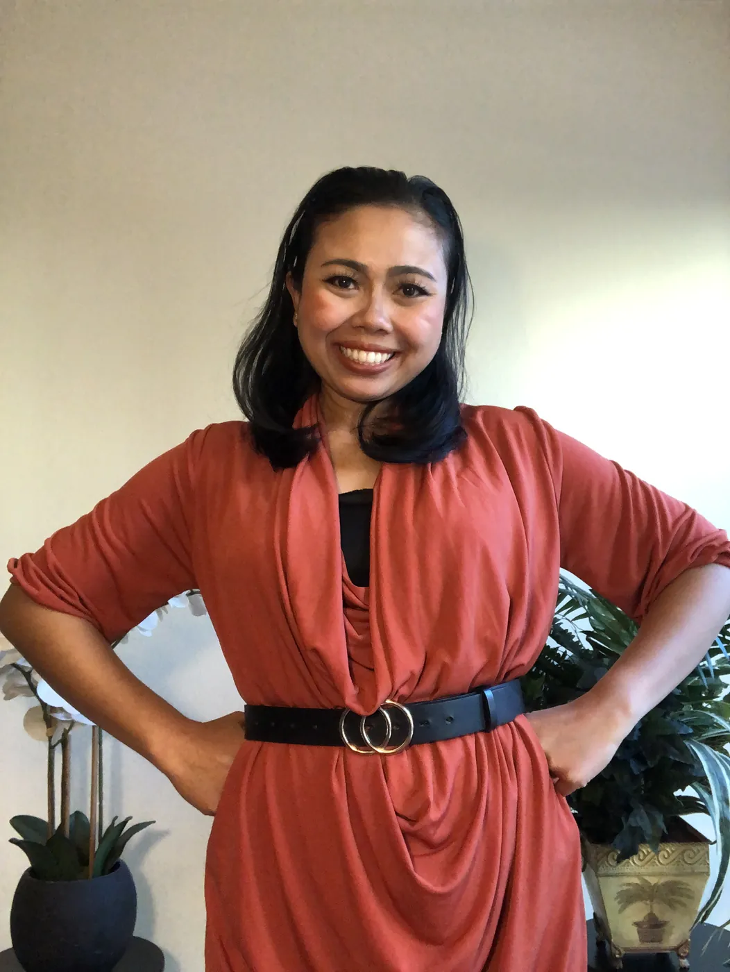 Krittaya smiling with her hands on her hips, wearing a rust-coloured dress