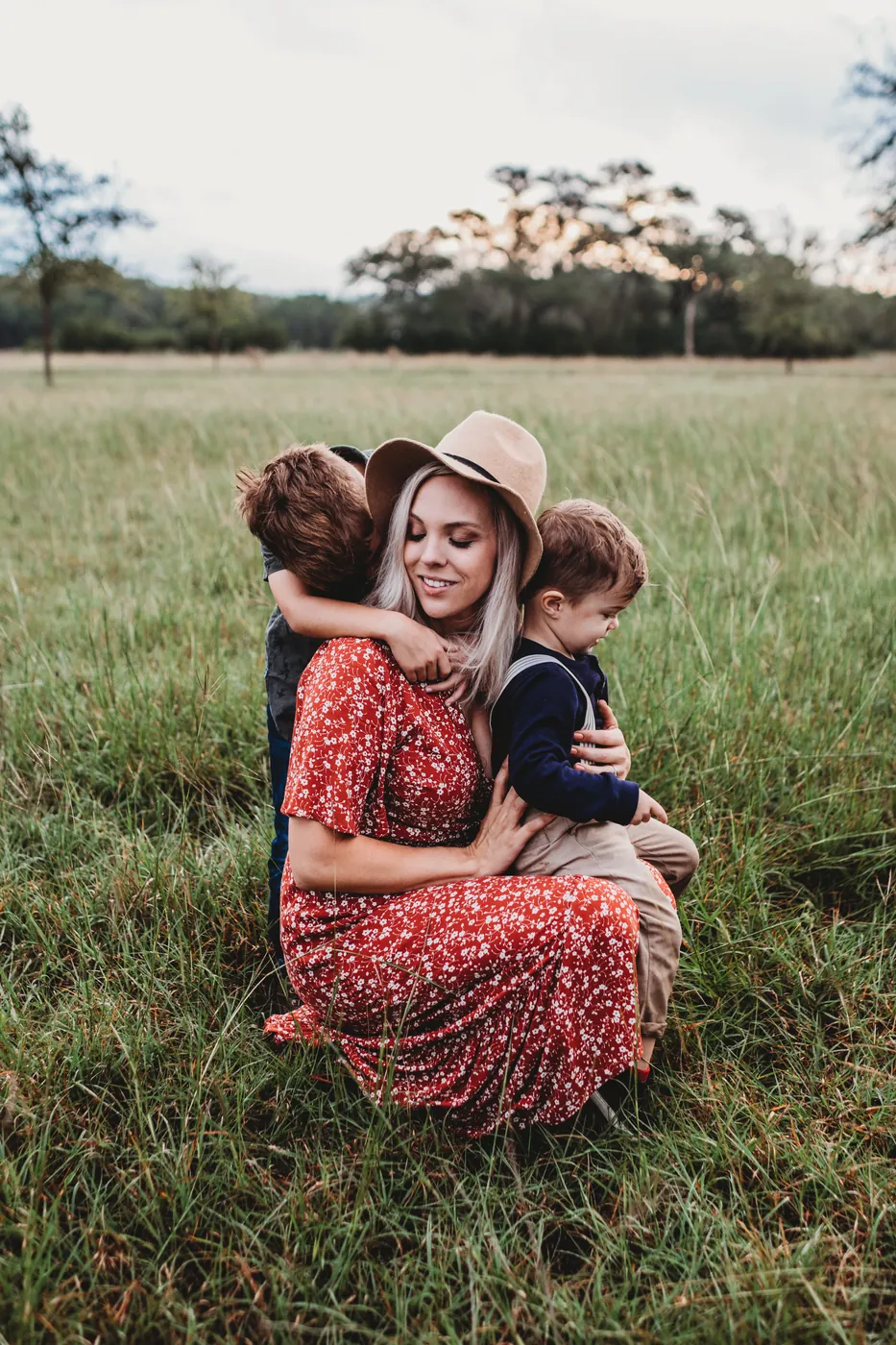 A mother hugging her two young children in a sunny field